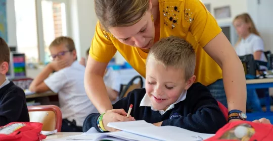 Une professeure des écoles accompagne un jeune élève dans un exercice